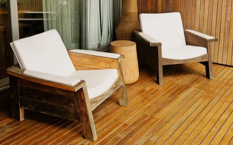 Deux fauteuils en bois à coussins blancs sur une terrasse en lames de bois huilées